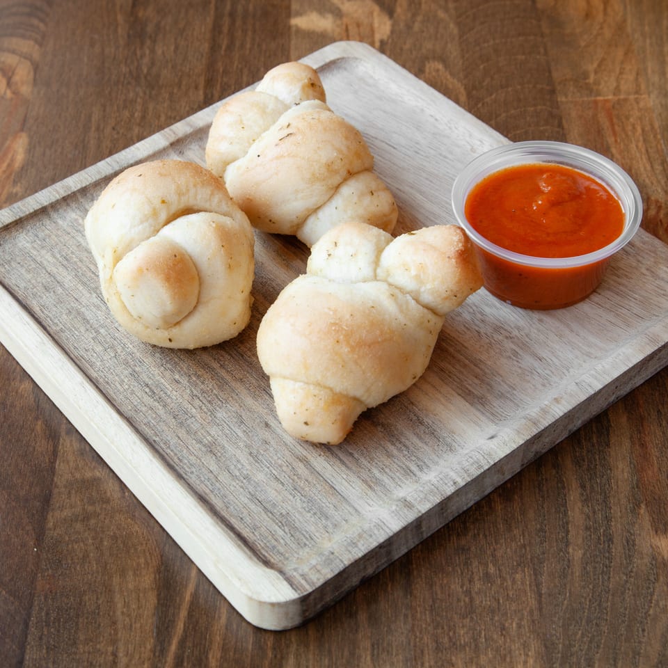 Golden-brown stuffed bread rolls arranged on a rustic wooden board with a cup of red dipping sauce.
